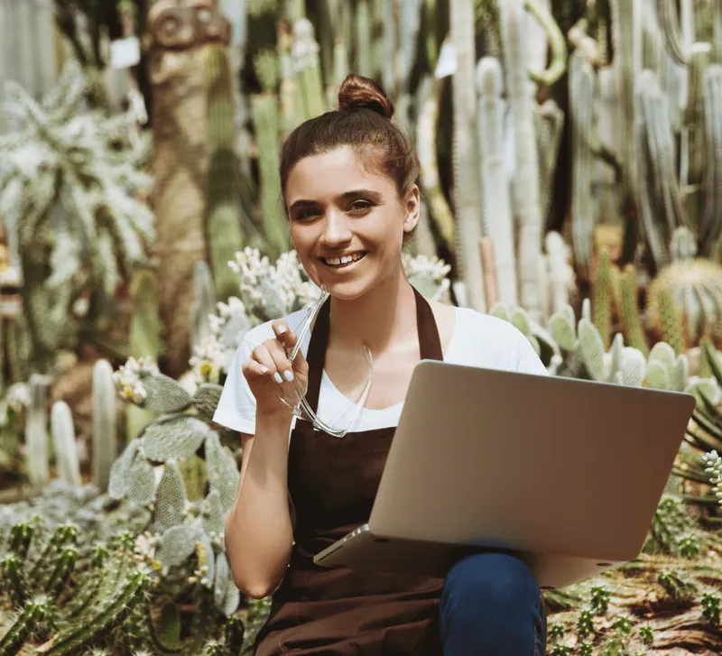 A smiling woman working on a laptop among plants